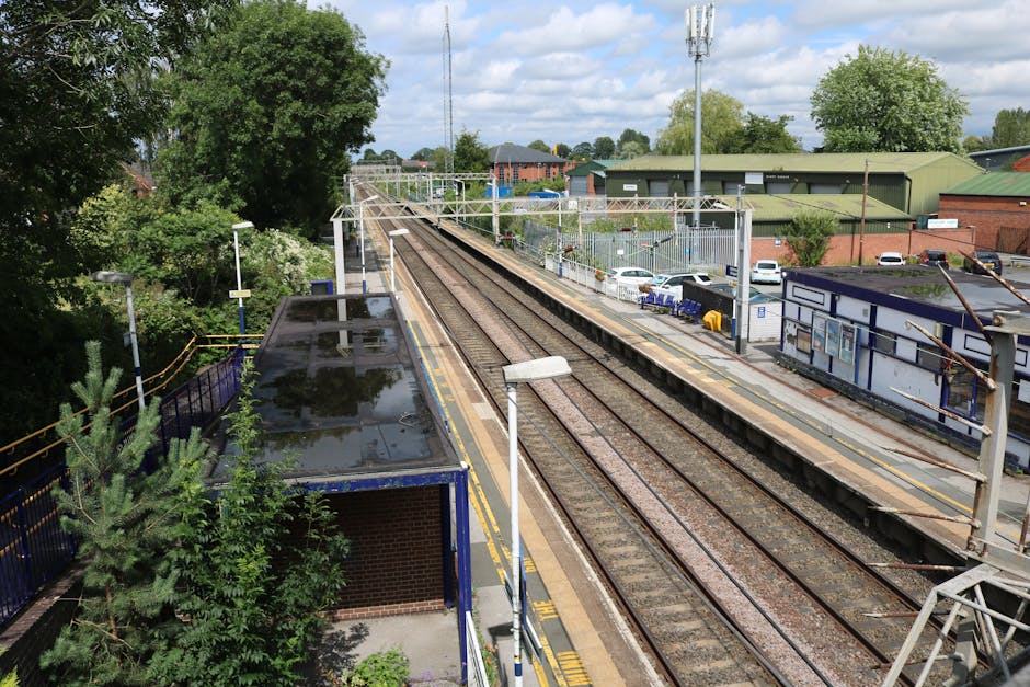 The entrance to Hanwell Station is framed by a brick archway with cream and brown bricks, leading into a walkway with tiled flooring. To the left and right of the arch, there are two black and white s